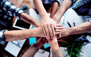 Hands stacking on one another in a show of collaboration/team work, in the workplace, showing a good Workplace Culture